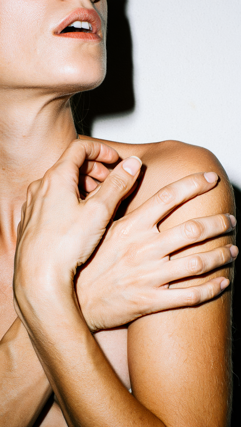 Close-up of a woman's hand touching her shoulder against a white background