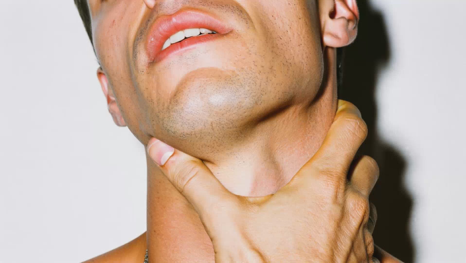 A close up video of a white man with short, dark hair, rubbing his neck and jaw with his hand