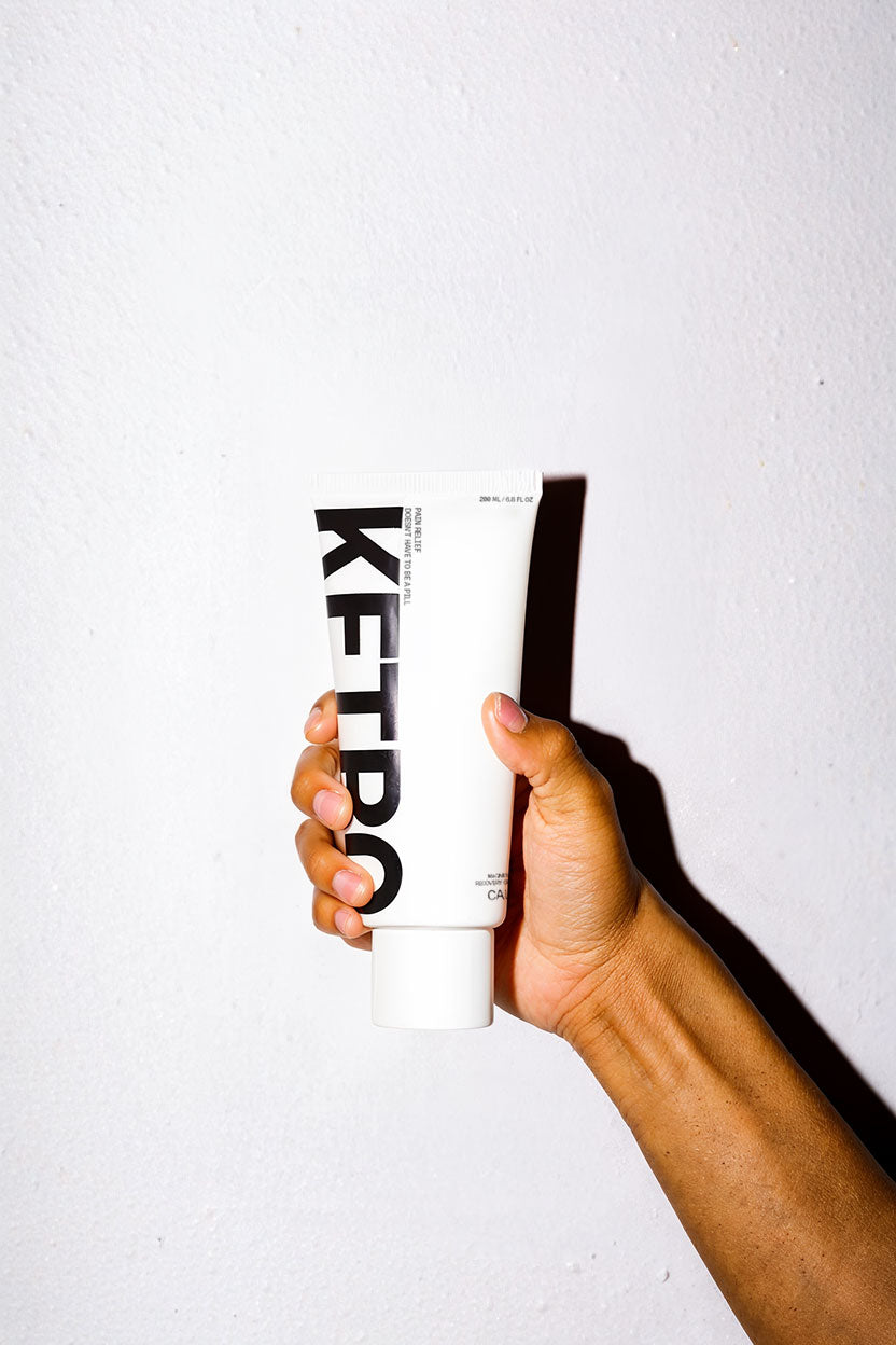 Hand holding a white tube with 'KETRO' branding against a light gray background