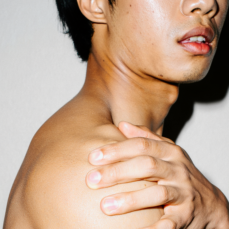 Close-up of a person with a hand on their shoulder against a plain background